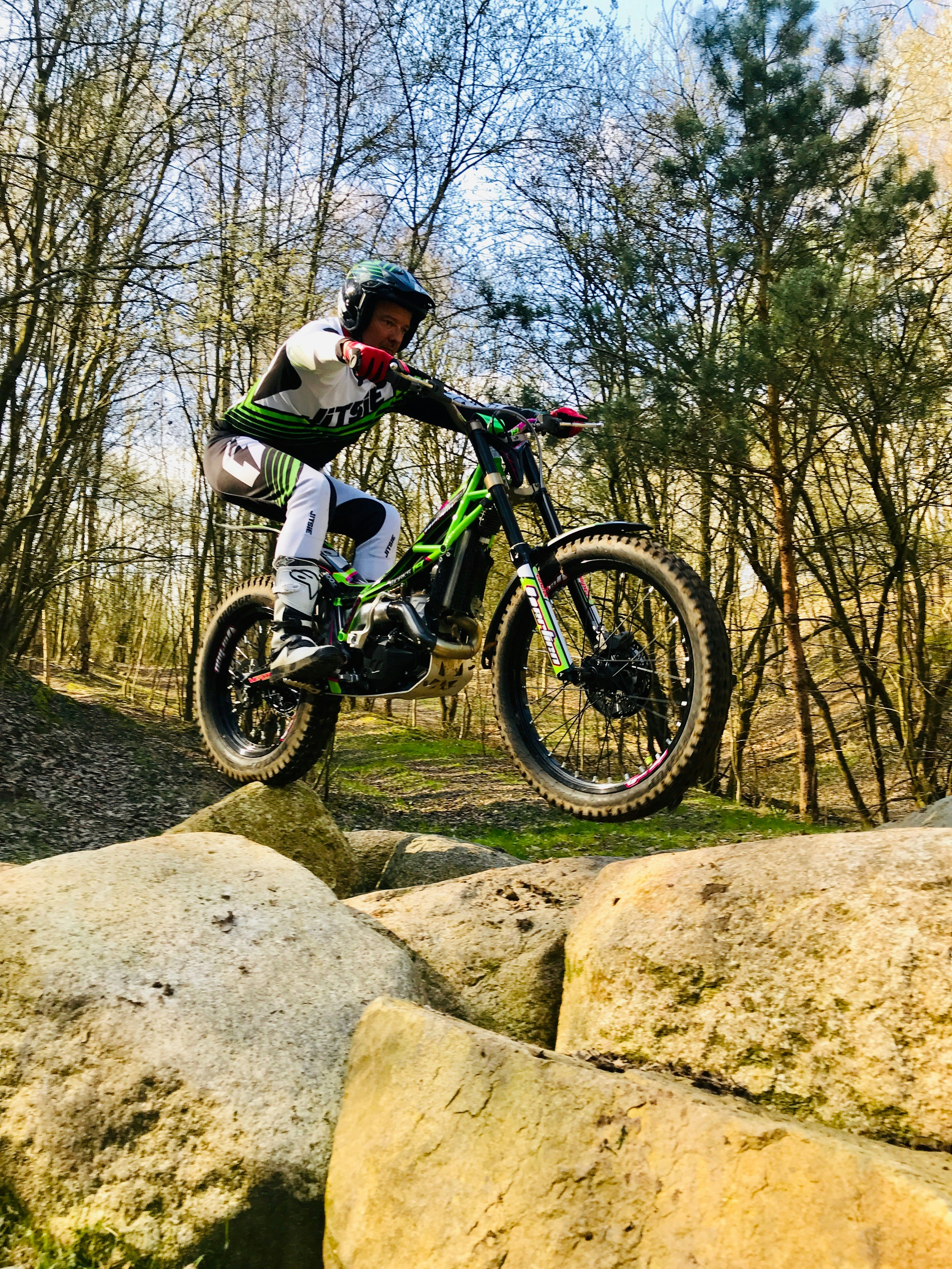 Trial motorcycle navigating rocks in a forest setting